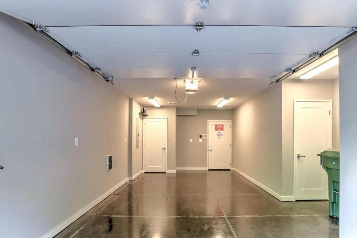 This image shows the private garage interior with visible garage doors, light fixtures, and entryway doors. The practical space is clearly intended for vehicle parking, storage, or as a workspace, and its clean, functional design highlights the convenience of having secure indoor parking.