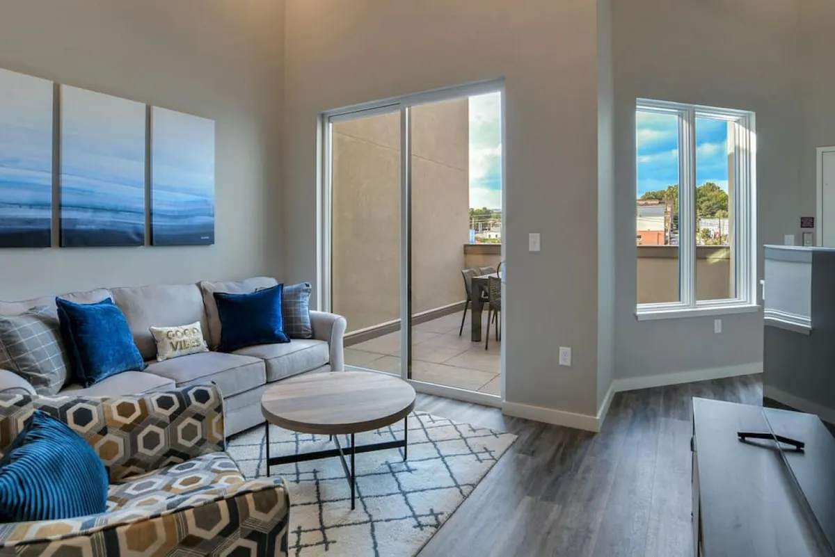 A bright, comfortable sitting area features a cozy sofa, coffee table, and large windows that frame a view of the city balcony. The relaxed setting is perfect for socializing, sipping morning coffee, or enjoying sunrise views from indoors before stepping onto the terrace.