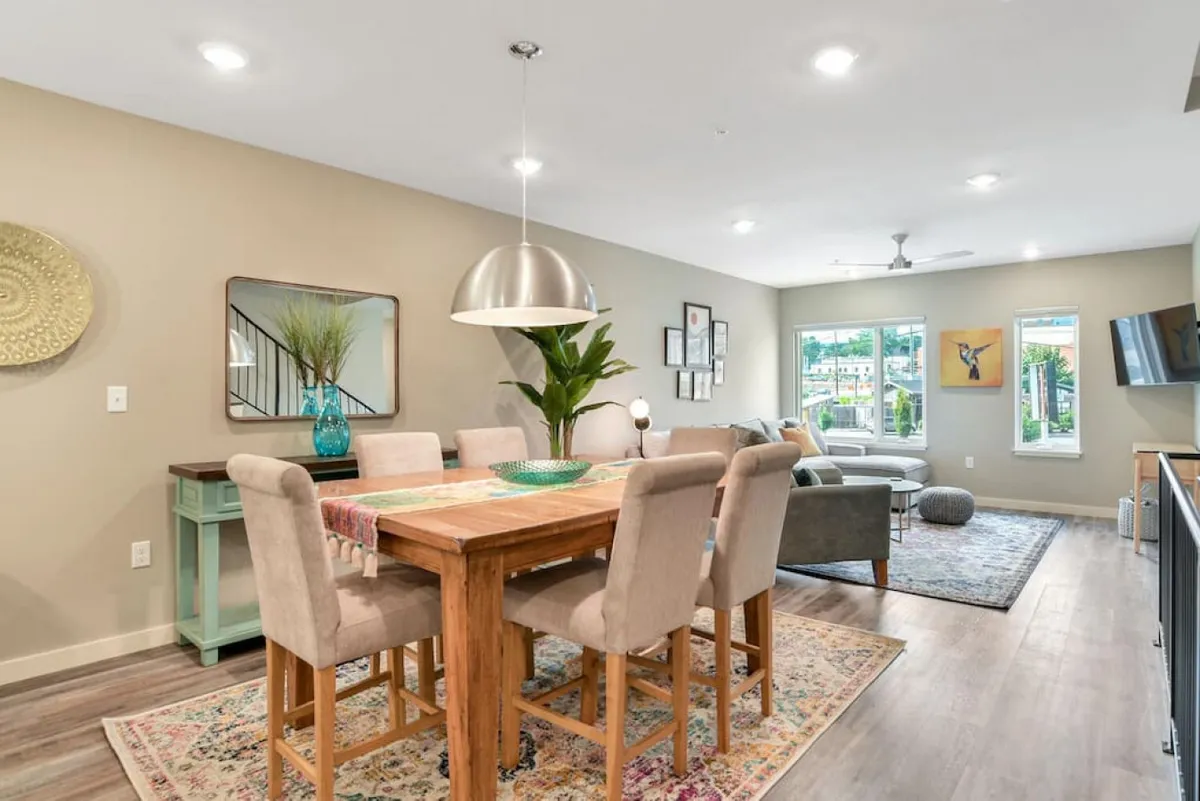 An inviting dining area with a large table surrounded by comfortable seating, decorative artwork on the walls, and expansive windows that suggest a connection to the outdoors. The space is set up for shared meals, games, or family conversations.