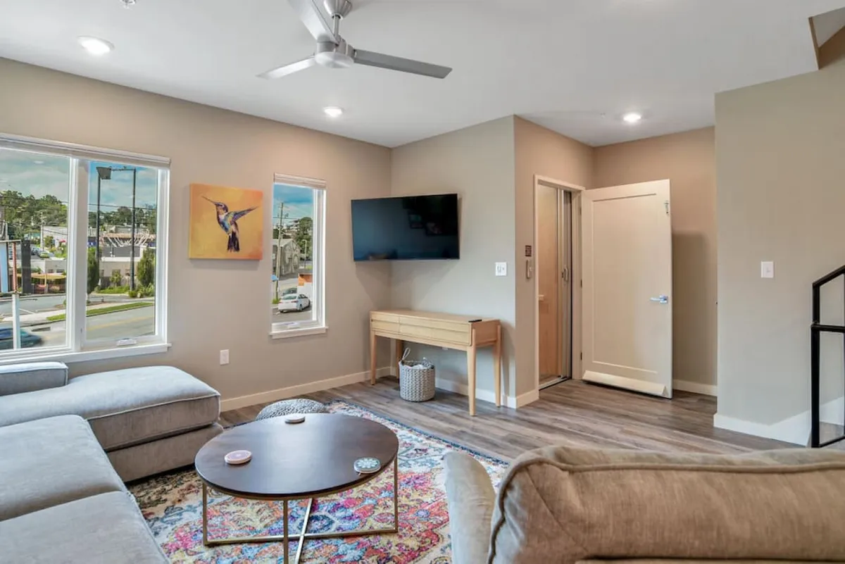 A stylish, contemporary living area featuring a comfortable sofa and coffee table, accented by modern artwork and a television. Large windows suggest a bright, urban setting, perfect for informal brainstorming or post-meeting relaxation.