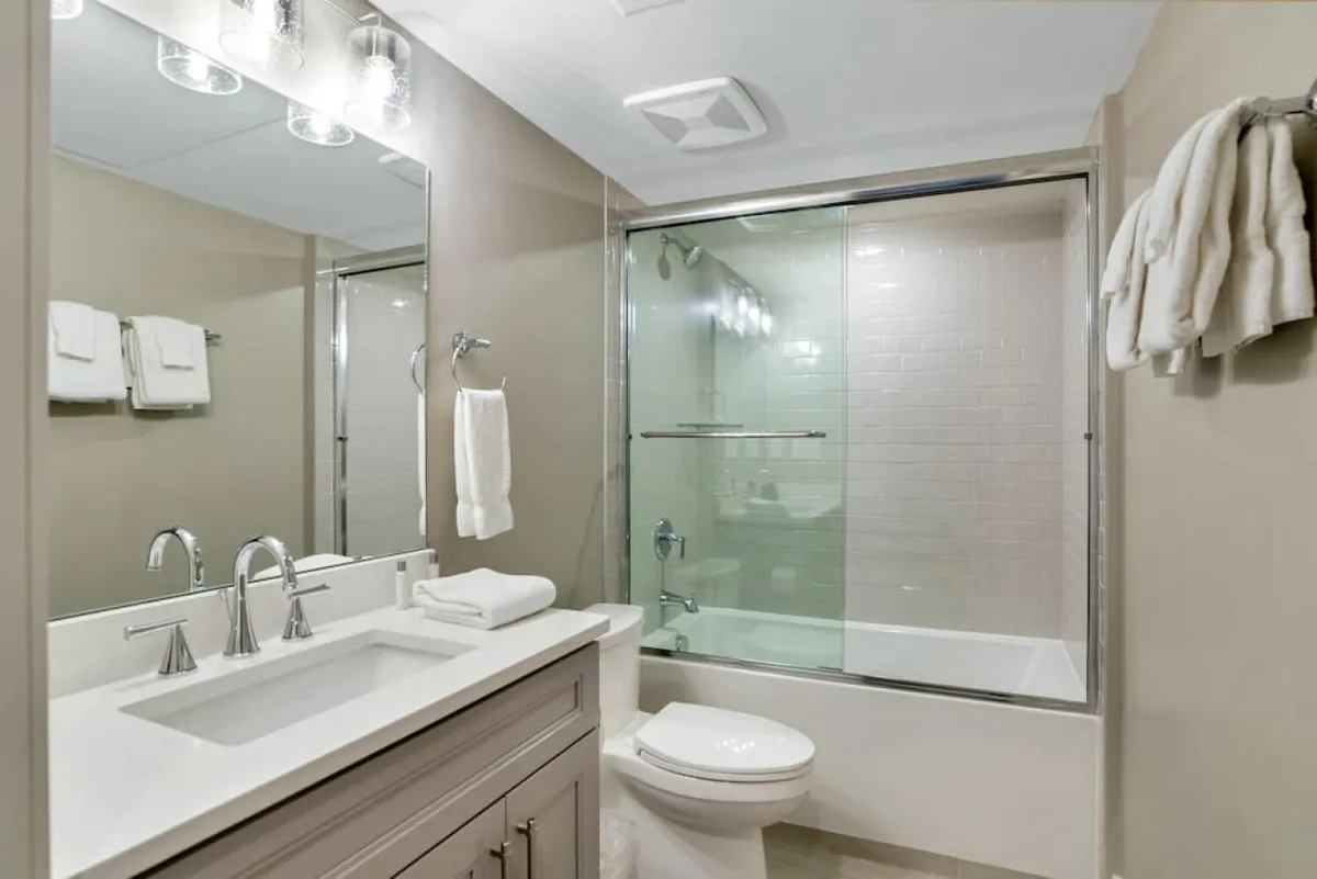 A modern bathroom with a sleek vanity, large mirror, and glass-enclosed shower. The space appears bright, fresh, and designed for comfort, inviting guests to enjoy either a refreshing shower or relaxing bath.