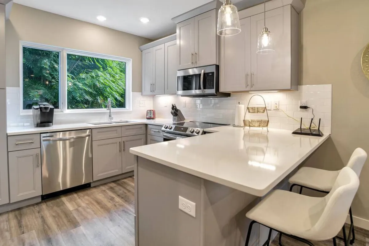 A bright, modern kitchen featuring a spacious island with bar stools, large windows flooding the room with natural sunlight, and sleek, stainless-steel appliances. The setup is perfect for casual family meals or gathering with friends for brunch.