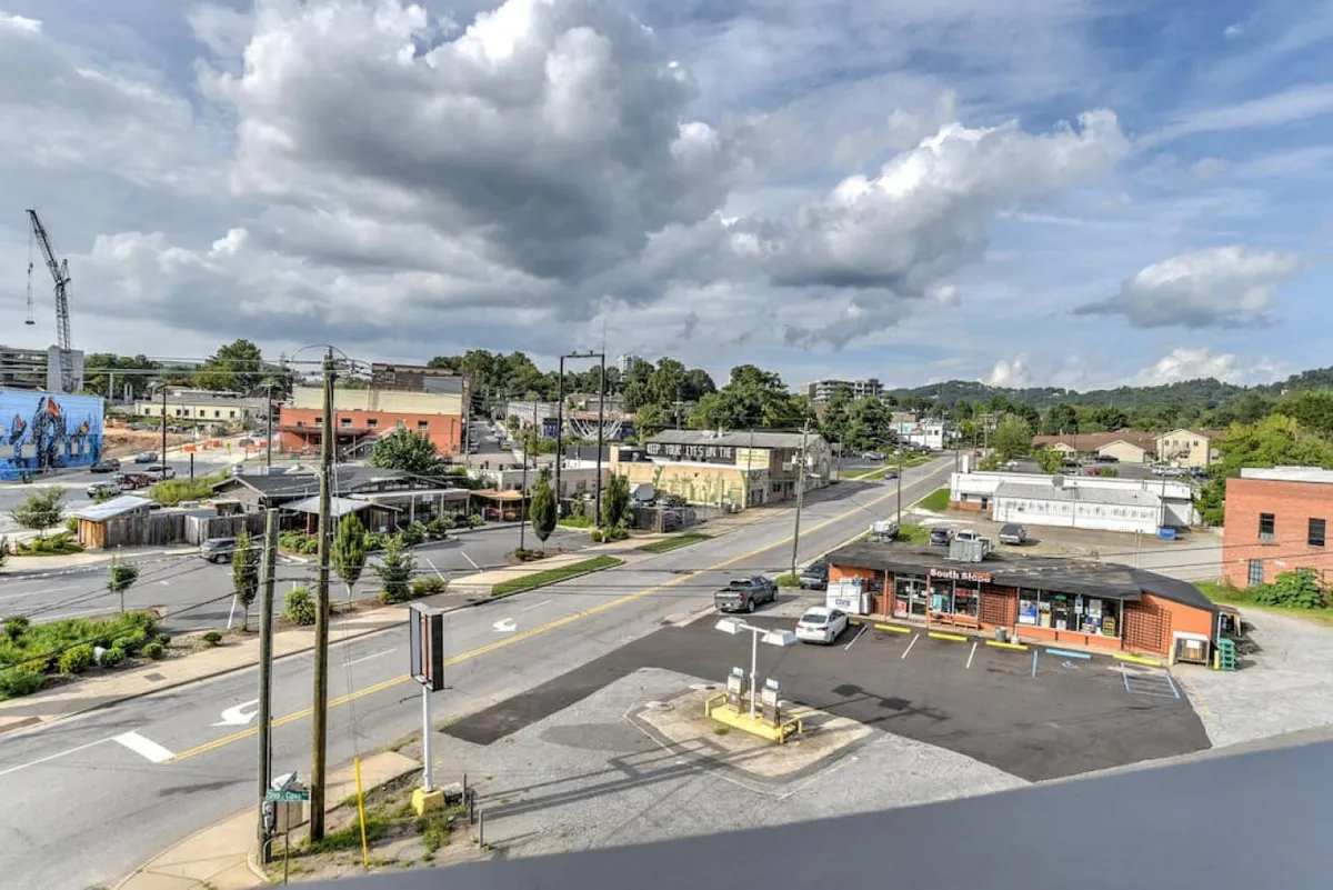 A dynamic street intersection in South Slope, framed by commercial buildings, a prominent billboard mural, and people moving between restaurants and shops. The scene buzzes with urban activity and city life.