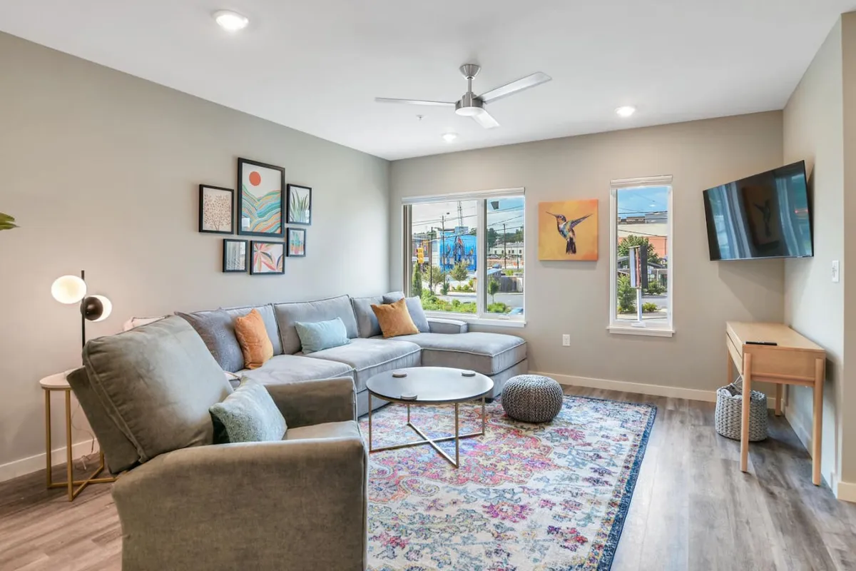 A cozy living space with a sofa and coffee table, accented by art and flanked by windows offering views and natural light. The layout is ideal for relaxing after a day of sightseeing or for enjoying sunset conversations with loved ones.