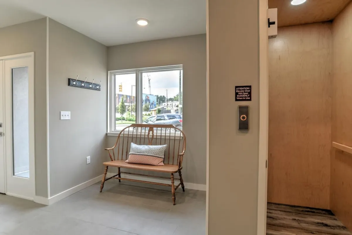 An interior view of the home's entryway featuring a bench, windows, and a visible elevator. The space is inviting, bright, and offers a clear first impression of the home's welcoming and sophisticated atmosphere. The elevator is a key focal point, directly supporting the section's emphasis on effortless access.